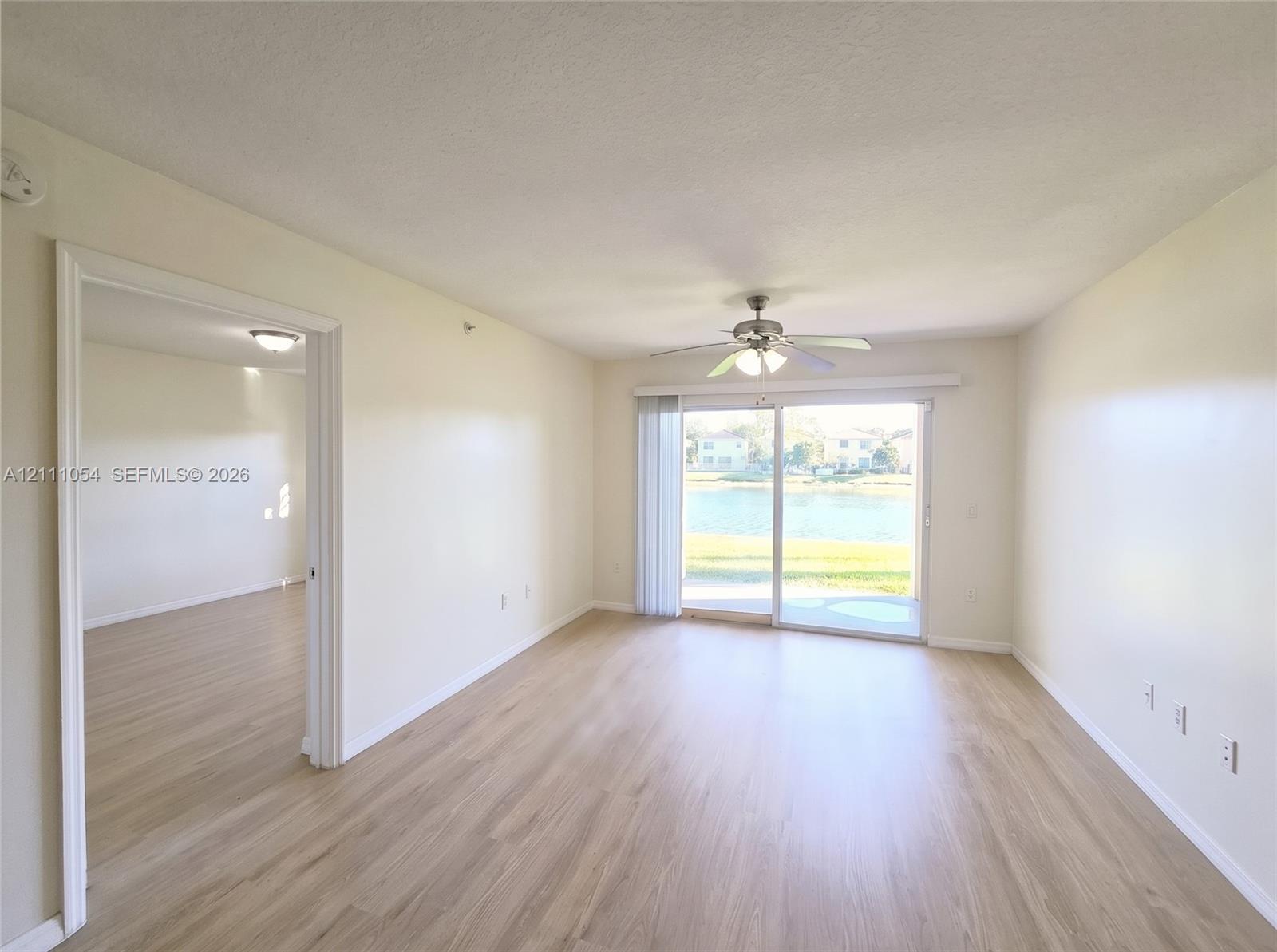 Living area featuring wood-finish flooring, sliding glass door, ceiling fan with integrated lighting, and neutral wall tones