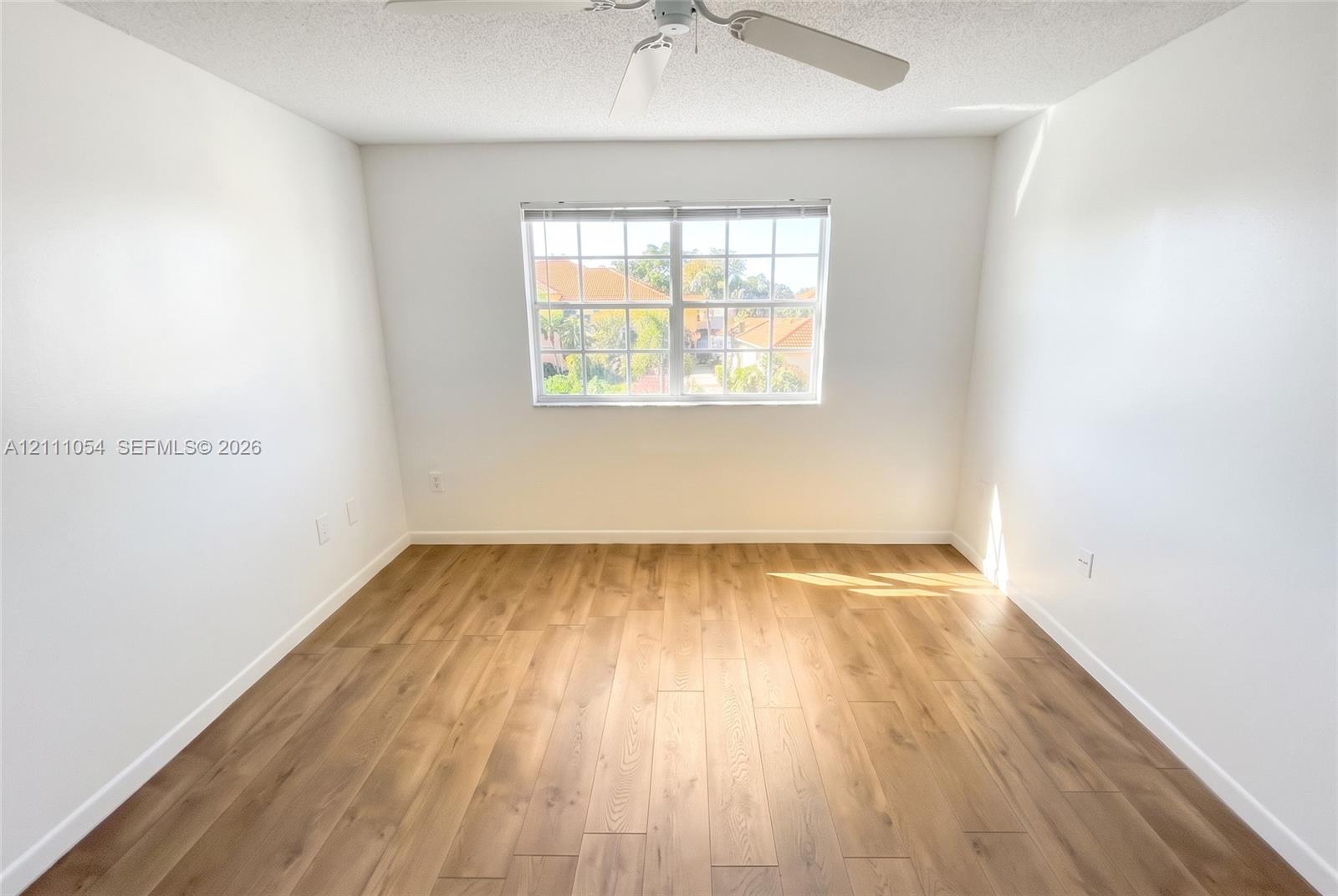 Room featuring wood-finish flooring, a multi-pane window, and a ceiling-mounted fan