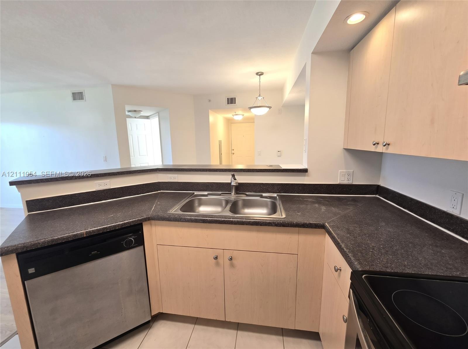 Kitchen featuring light-finish cabinetry, dark solid-surface countertops, stainless steel dual-basin sink, and recessed lighting
