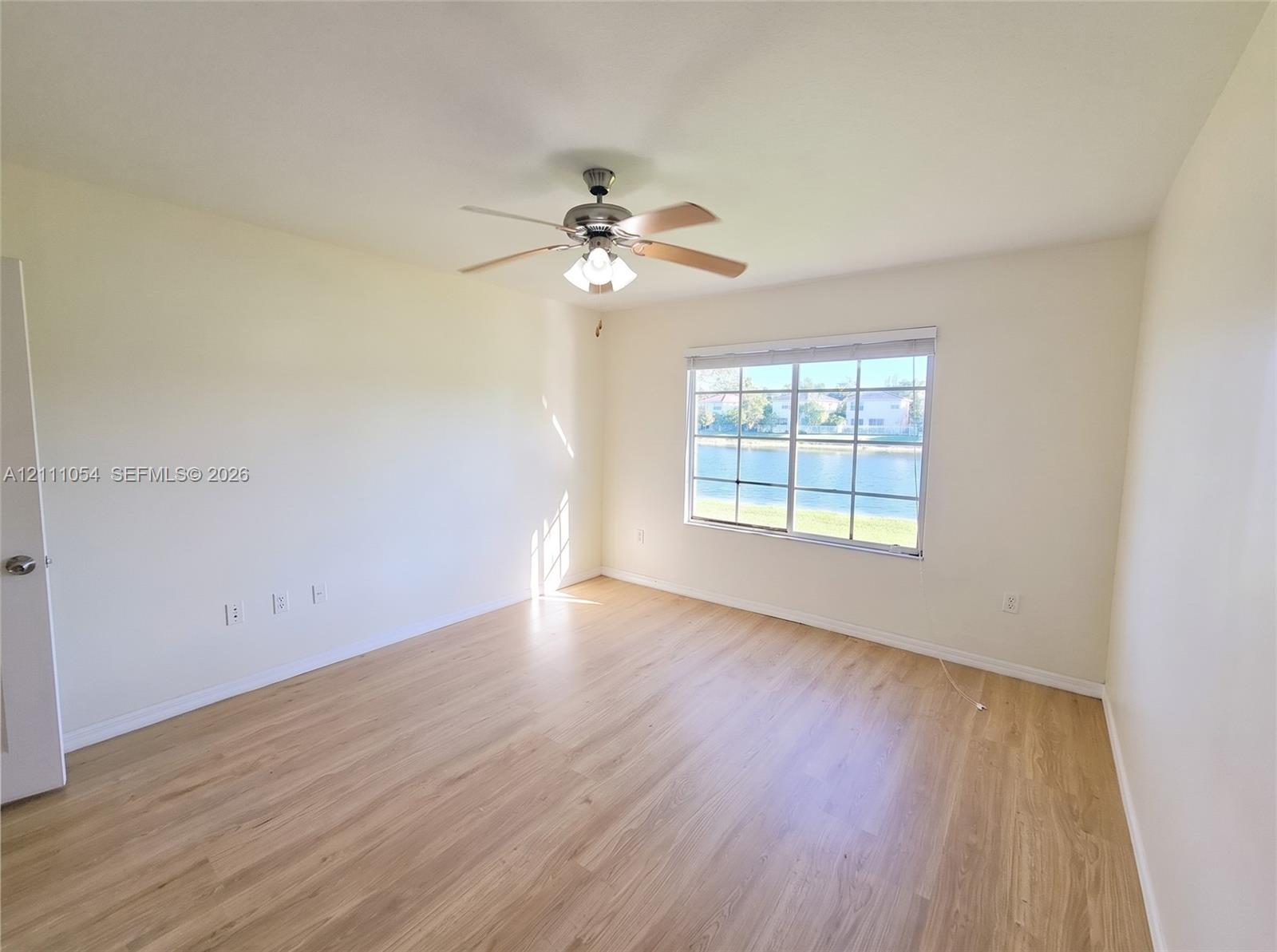 Interior space featuring wood-finish flooring, a ceiling fan with integrated lighting, and a grid-pane window overlooking a water feature