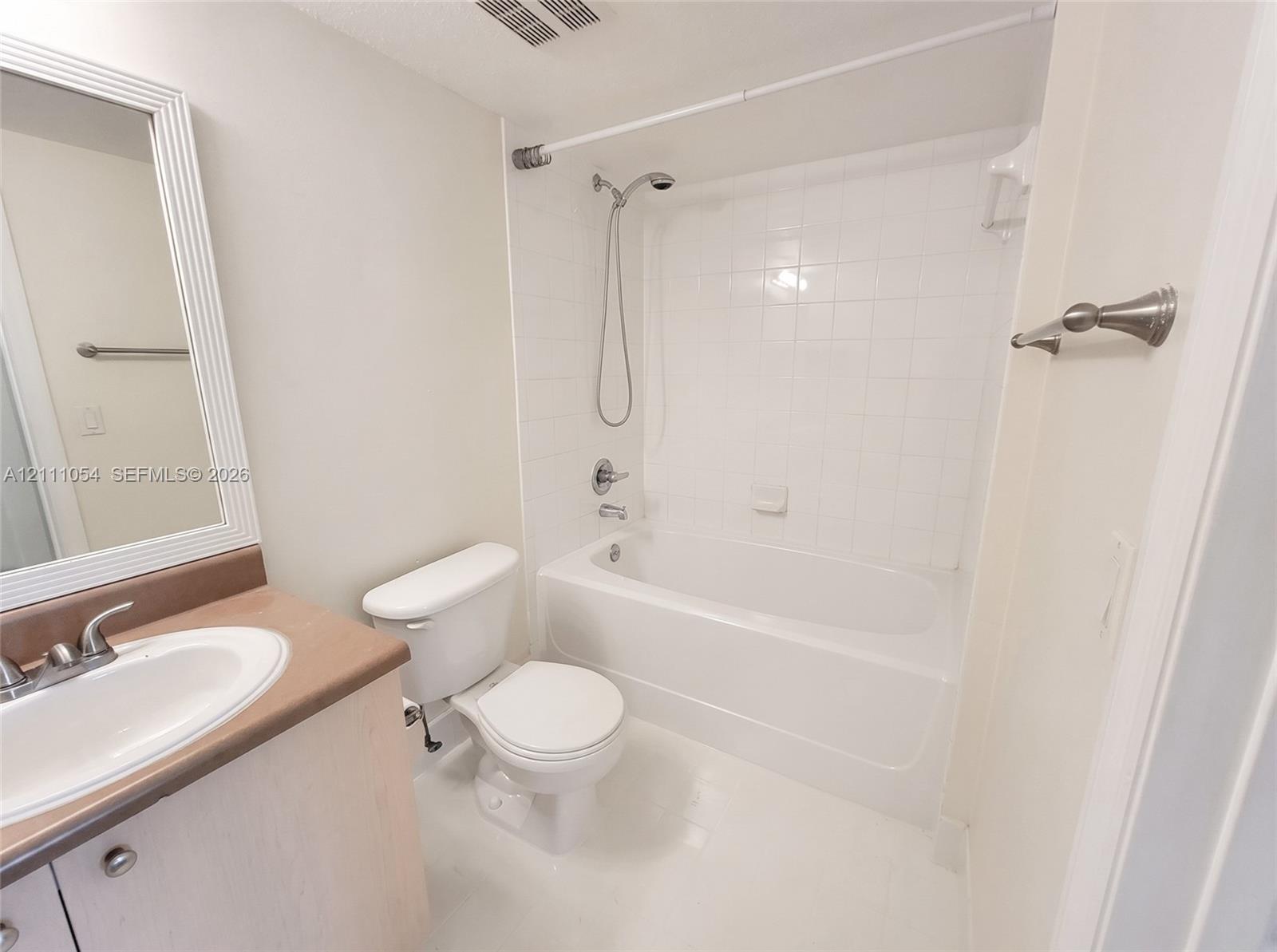 Bathroom featuring a vanity with a solid-surface countertop, an integrated sink with a dual-handle faucet, a white porcelain toilet, and a shower-tub combination with white tile surround and a handheld shower head