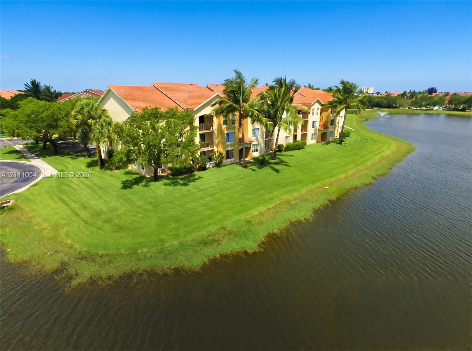 Multi-story residential building featuring a tile roof, stucco exterior, private balconies, and landscaped grounds positioned along a lakefront