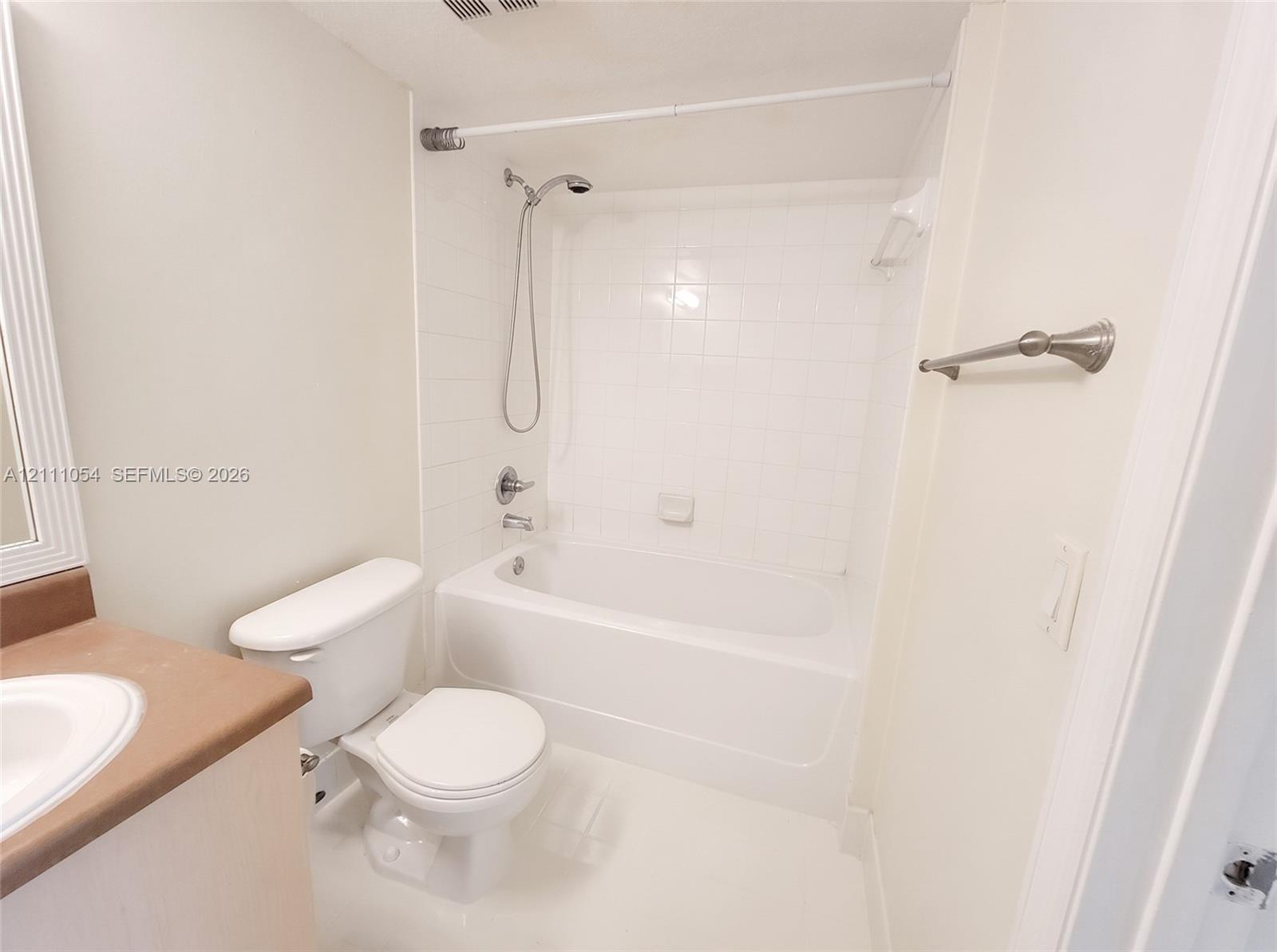 Bathroom featuring a white bathtub with tile surround, handheld shower fixture, vanity with integrated basin, and brushed-finish towel bar