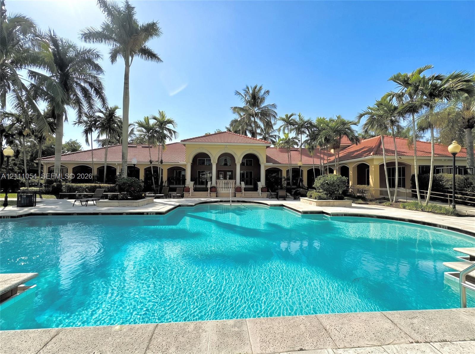 Expansive swimming pool with stone coping, arched architectural detailing, tile roof, and mature palm landscaping