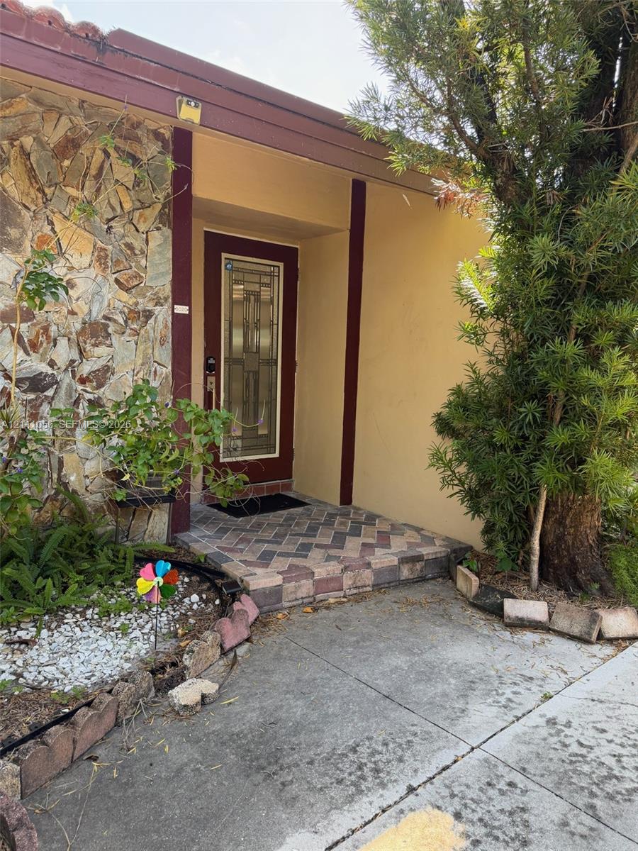 Entryway featuring a stone-veneer exterior facade, herringbone-patterned brick paver landing, and a decorative glass-panel front door