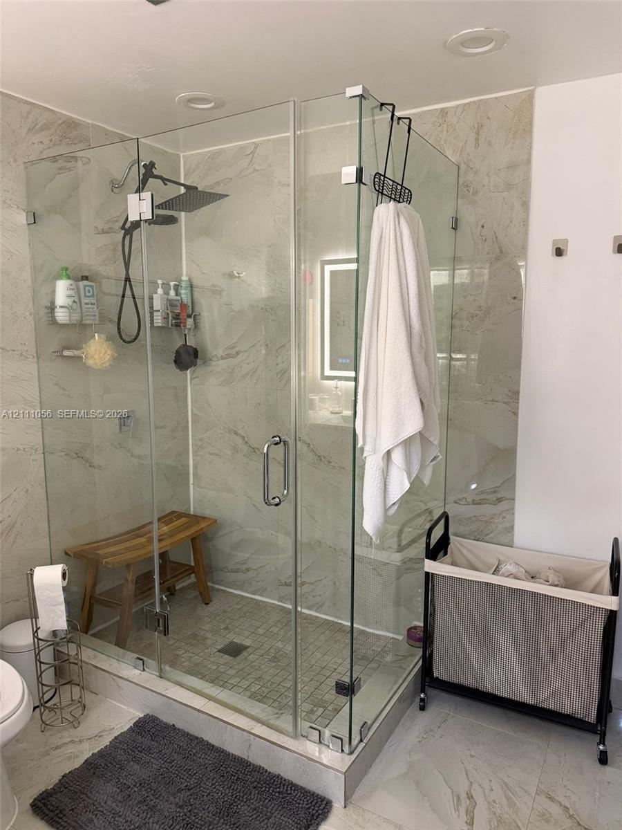 Walk-in shower featuring glass panel enclosure, large-format tile surround, rainfall shower head, and built-in bench seating