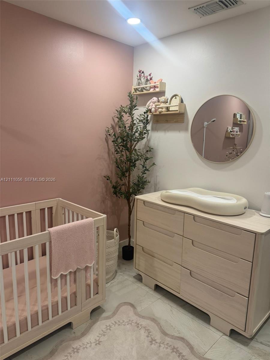 Room featuring an accent wall in a muted rose tone, neutral light-finish wood-tone built-in cabinetry, large-format tile flooring, a circular wall-mounted mirror, and recessed lighting