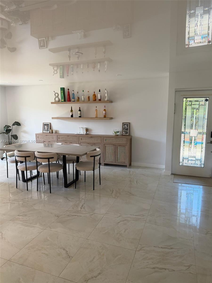 Large-format tiled flooring throughout, built-in wooden cabinetry with textured door fronts, dual wall-mounted floating wood shelves, and a front entry door featuring decorative geometric glass panes