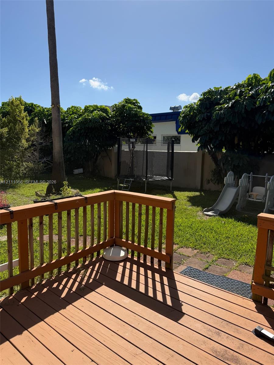 Raised wooden deck with railing overlooking a lawn area enclosed by a masonry perimeter wall and mature landscaping