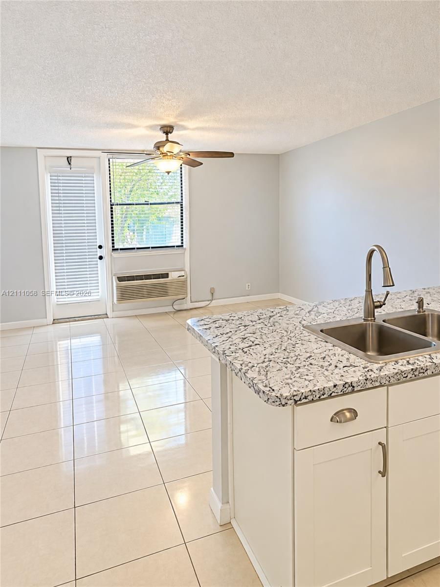 Kitchen island featuring a stone-look countertop, undermount double-basin stainless steel sink, polished chrome faucet, white Shaker-style cabinetry, and light-toned tile flooring Kitchen island featuring a stone-look countertop, undermount double-basin stainless steel sink, polished chrome faucet, white Shaker-style cabinetry, and light-toned tile flooring