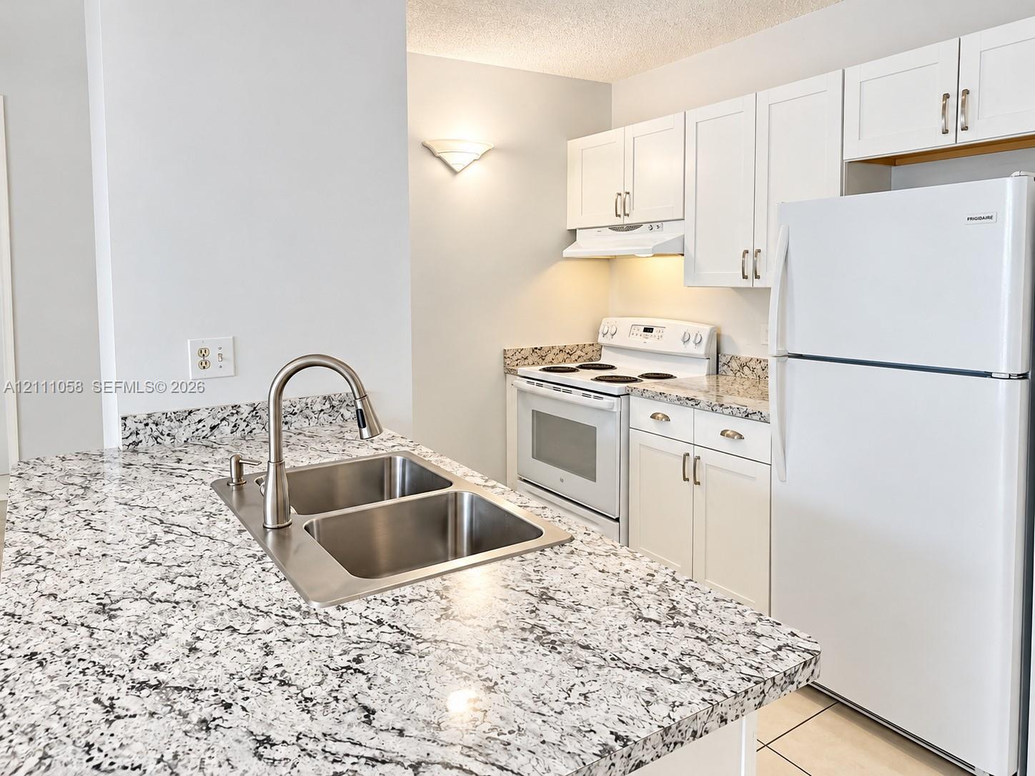 Kitchen featuring speckled stone countertops, dual-basin stainless steel sink with a high-arch faucet, white cabinetry, and matching white appliances Kitchen featuring speckled stone countertops, dual-basin stainless steel sink with a high-arch faucet, white cabinetry, and matching white appliances