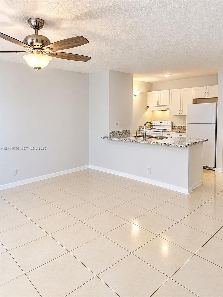 Ceramic tile flooring, breakfast bar with stone-finish countertop, white shaker-style cabinetry, and brushed nickel ceiling fan Ceramic tile flooring, breakfast bar with stone-finish countertop, white shaker-style cabinetry, and brushed nickel ceiling fan