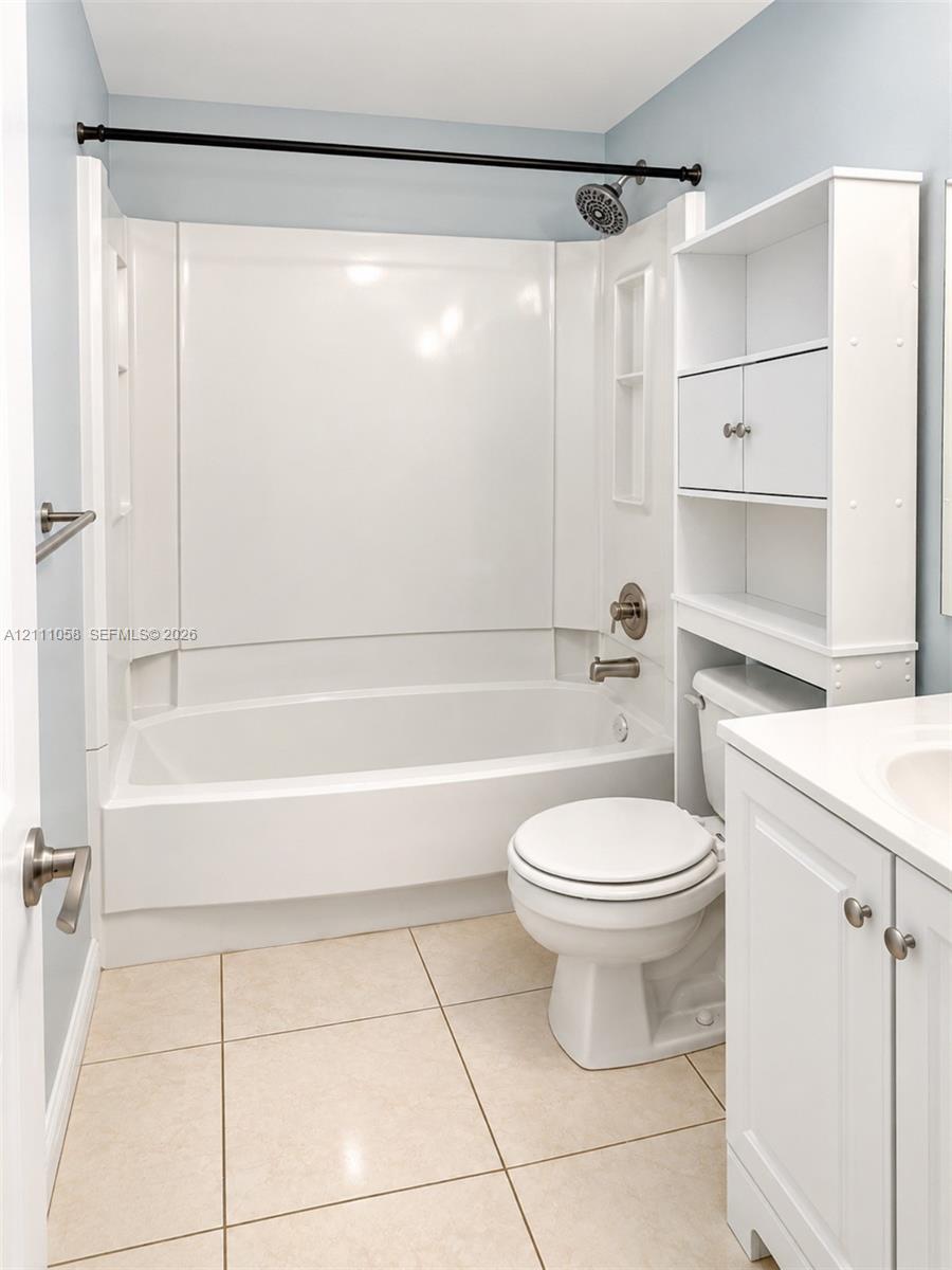 Full-bathroom featuring a tub-shower combination with integrated shelving, white vanity with stone-style countertop, large-format tile flooring, and built-in vertical storage unit Full-bathroom featuring a tub-shower combination with integrated shelving, white vanity with stone-style countertop, large-format tile flooring, and built-in vertical storage unit