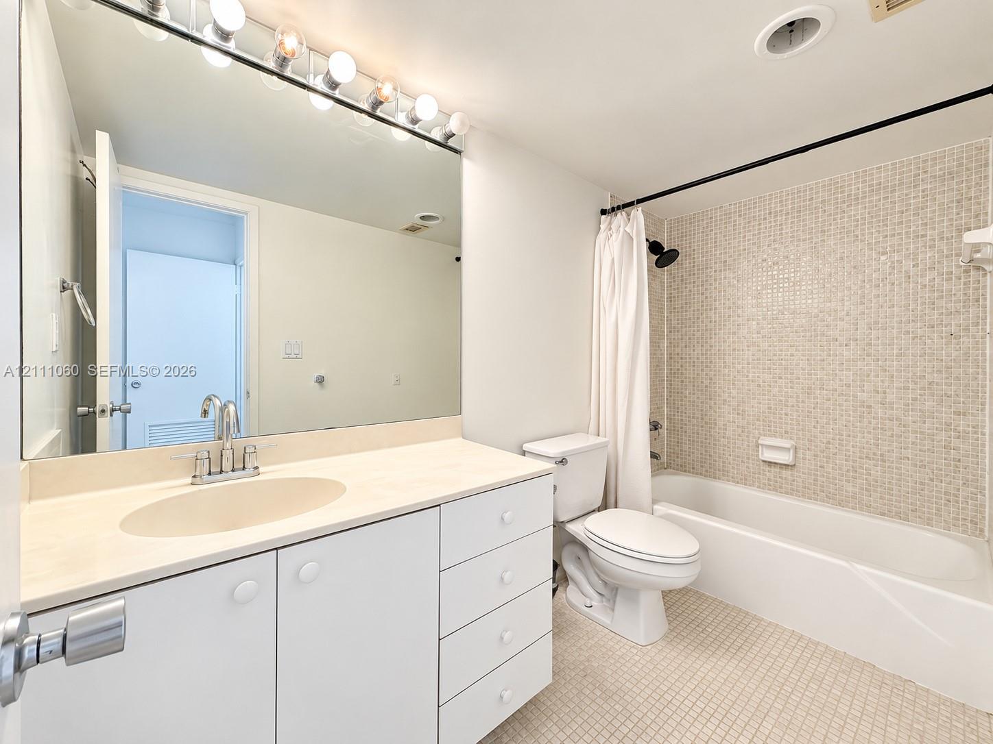 Bathroom featuring a vanity with integrated sink, expansive wall-to-wall mirror, built-in cabinetry, mosaic wall tile within the shower enclosure, and mosaic tile flooring