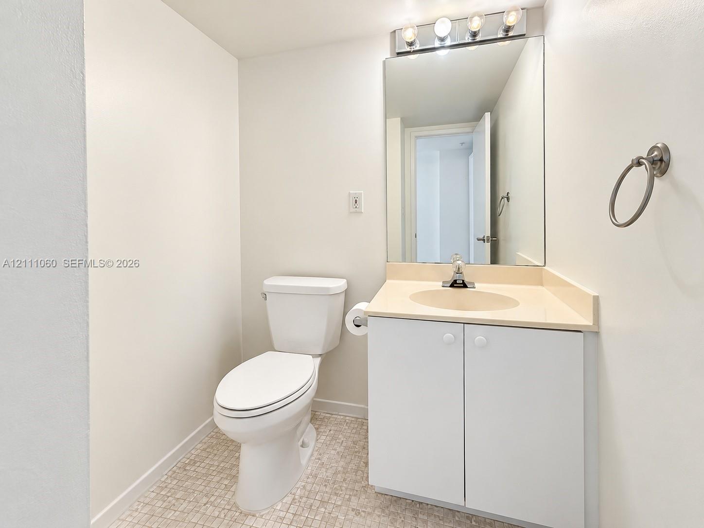 Vanity with an integrated sink and countertop, white cabinetry, a wall-mounted mirror, four-bulb vanity lighting, and tiled flooring