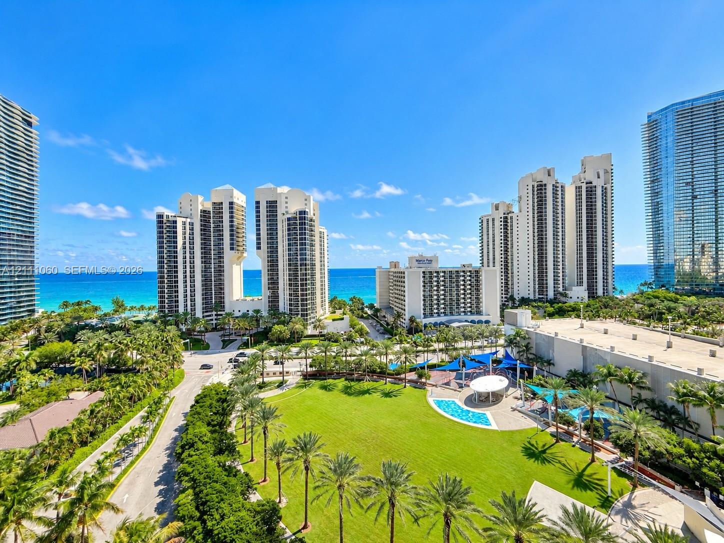 High-rise residential surroundings featuring mature palm landscaping, manicured lawn areas, a communal swimming pool, and proximity to the coastline High-rise residential surroundings featuring mature palm landscaping, manicured lawn areas, a communal swimming pool, and proximity to the coastline