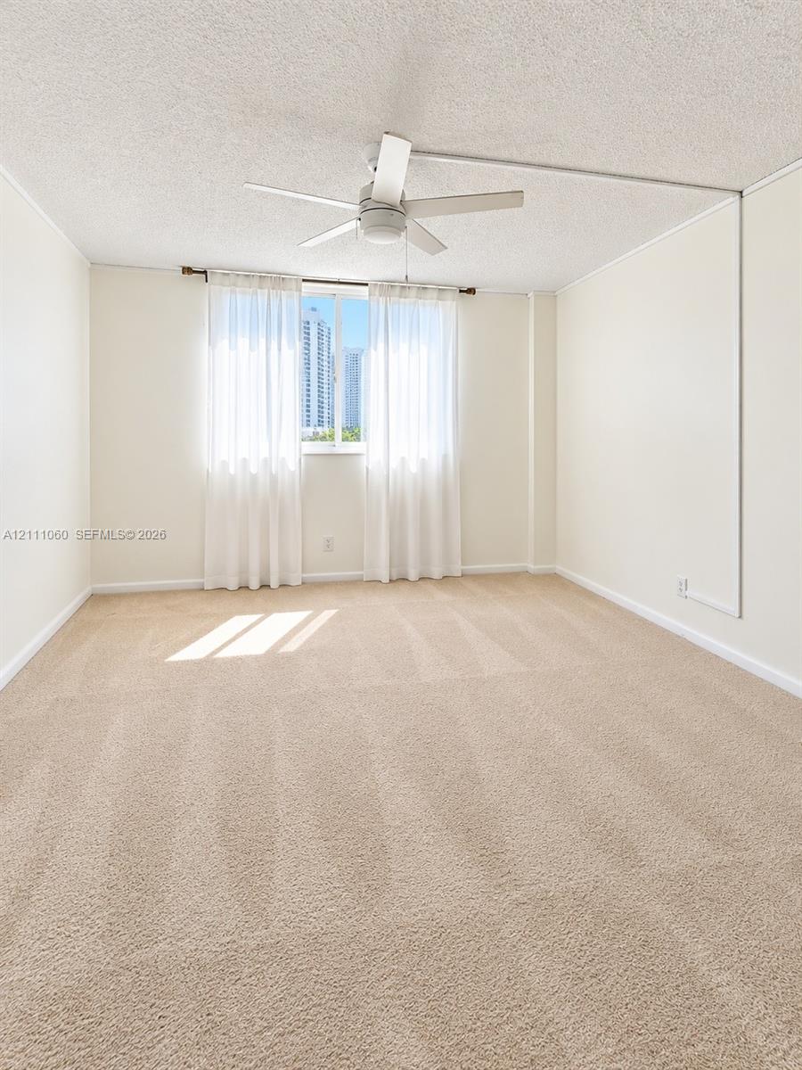 Neutral-toned carpeting, textured ceiling, and a ceiling-mounted fan with integrated light fixture