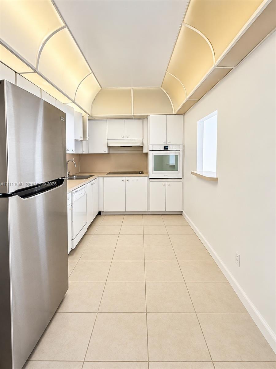 Kitchen featuring white cabinetry, stainless steel refrigerator, built-in wall oven, tile flooring, and barrel vault ceiling detail