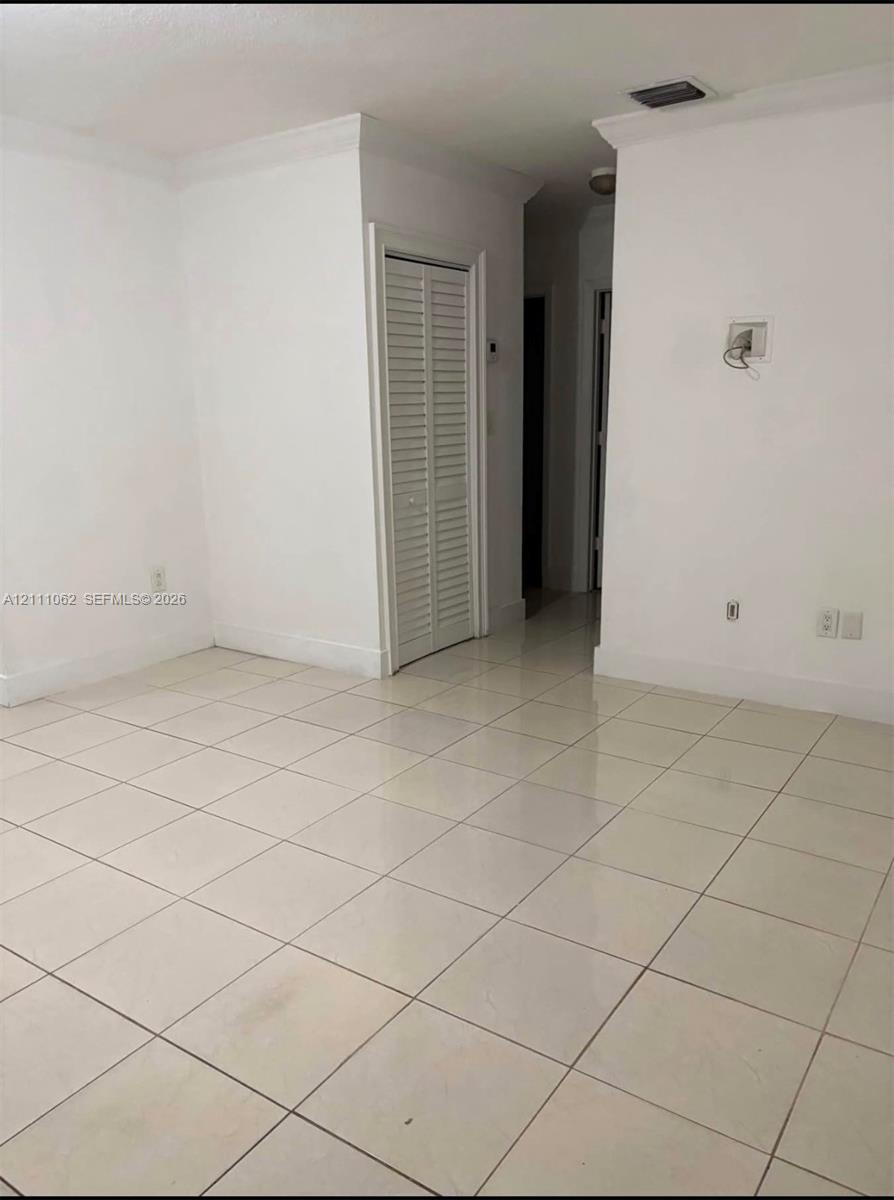 Neutral-toned tile flooring, crown molding, and louvered closet doors