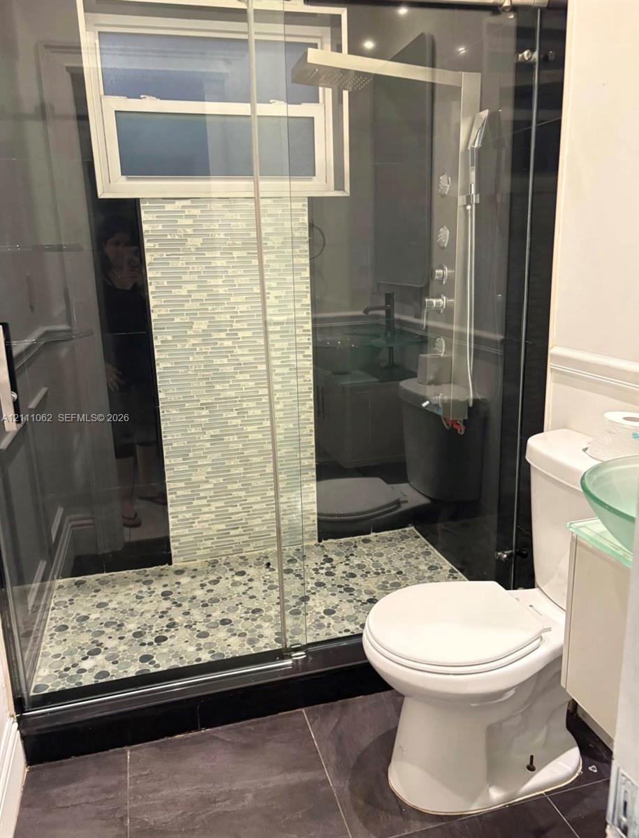 Walk-in shower featuring a glass enclosure, pebble-stone flooring, multi-head rainfall shower system, and a decorative mosaic tile accent wall