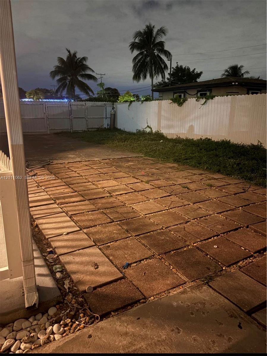 Rear patio featuring concrete pavers, enclosed by a white privacy fence with double-gate access