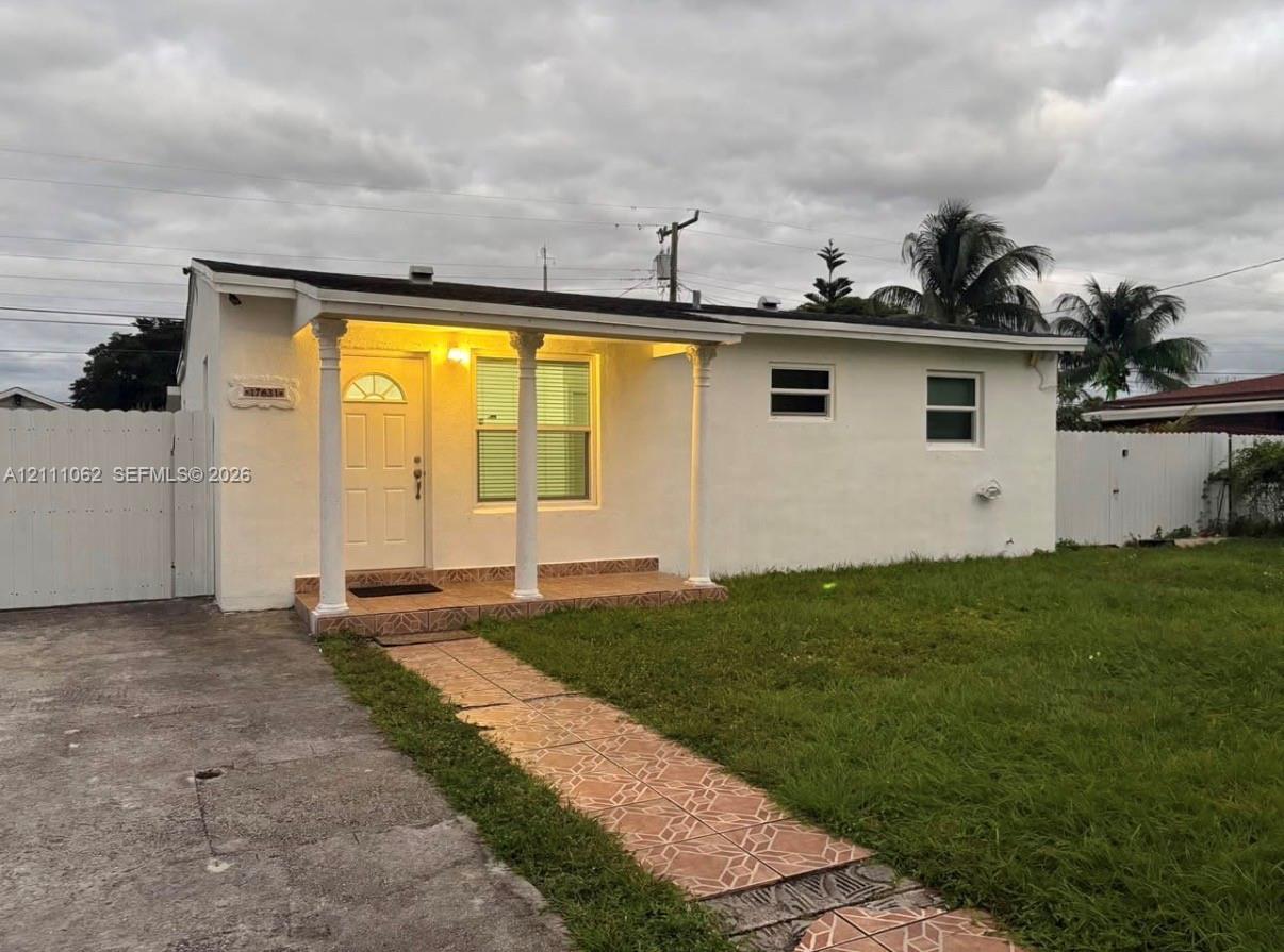 Stucco exterior featuring a covered front porch with decorative columns, a tiled walkway, and full perimeter privacy fencing Stucco exterior featuring a covered front porch with decorative columns, a tiled walkway, and full perimeter privacy fencing