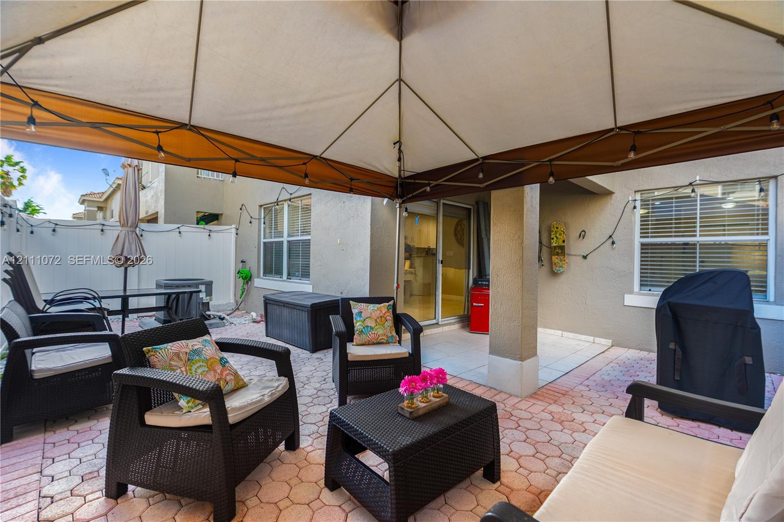 Covered patio area featuring patterned concrete pavers, neutral exterior stucco finish, and sliding glass door entry