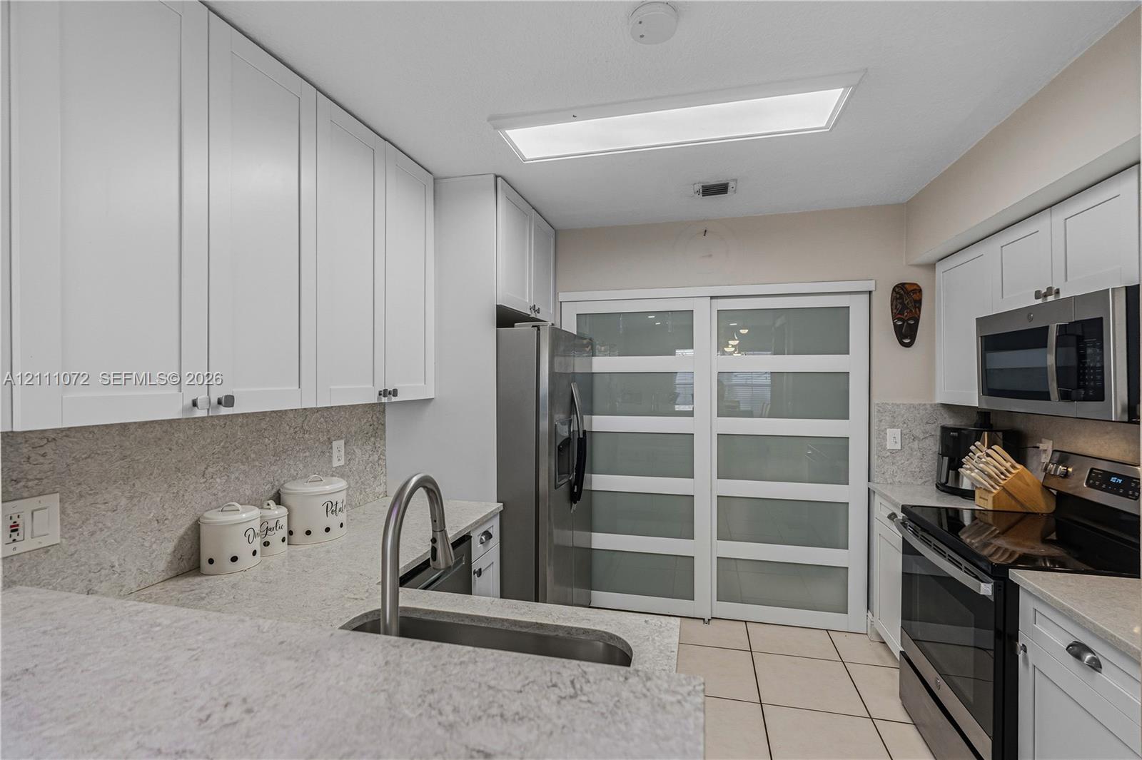 Kitchen featuring white shaker-style cabinetry, stone-finish countertops, stainless steel appliances, a high-arc pull-down faucet, and frosted glass sliding panels