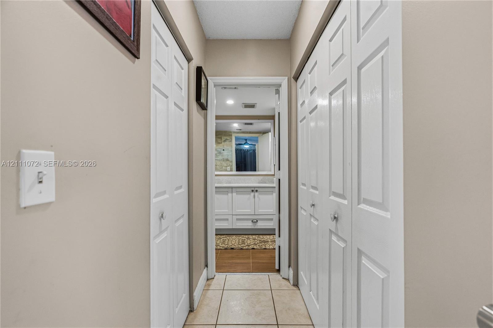 Hallway featuring dual sets of white bi-fold closet doors and neutral-tone tile flooring