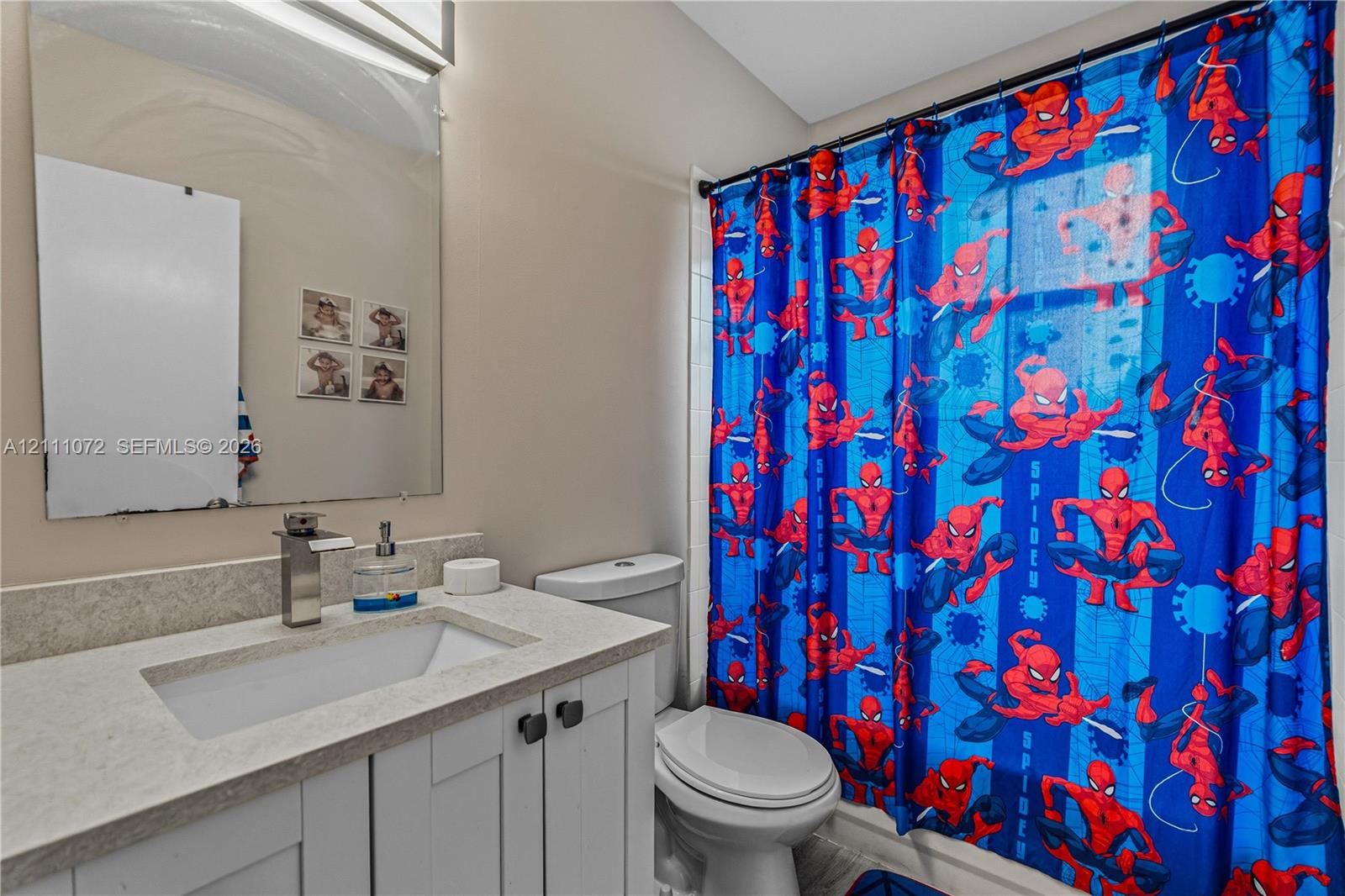 Bathroom featuring a light-toned vanity with an integrated rectangular sink, stone-composite countertop, wall-mounted mirror, and a single-handle chrome faucet