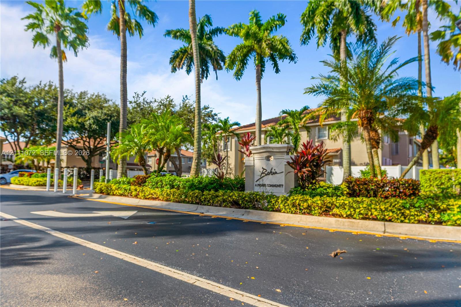 Community entrance signage featuring stone monument masonry, mature palm trees, and manicured shrubbery