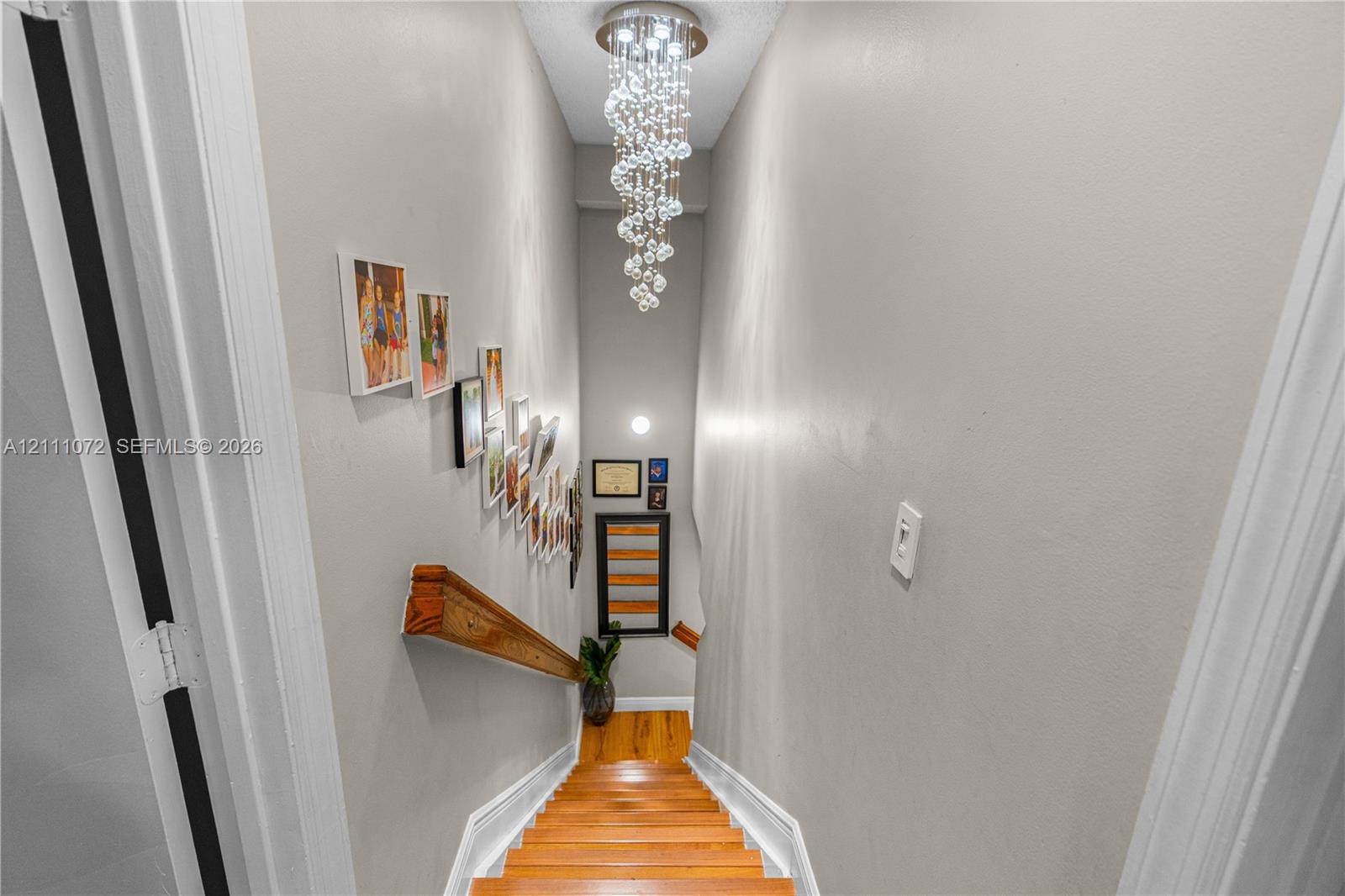 Staircase featuring wood-finish treads, a wood-finish handrail, and a tiered crystal chandelier