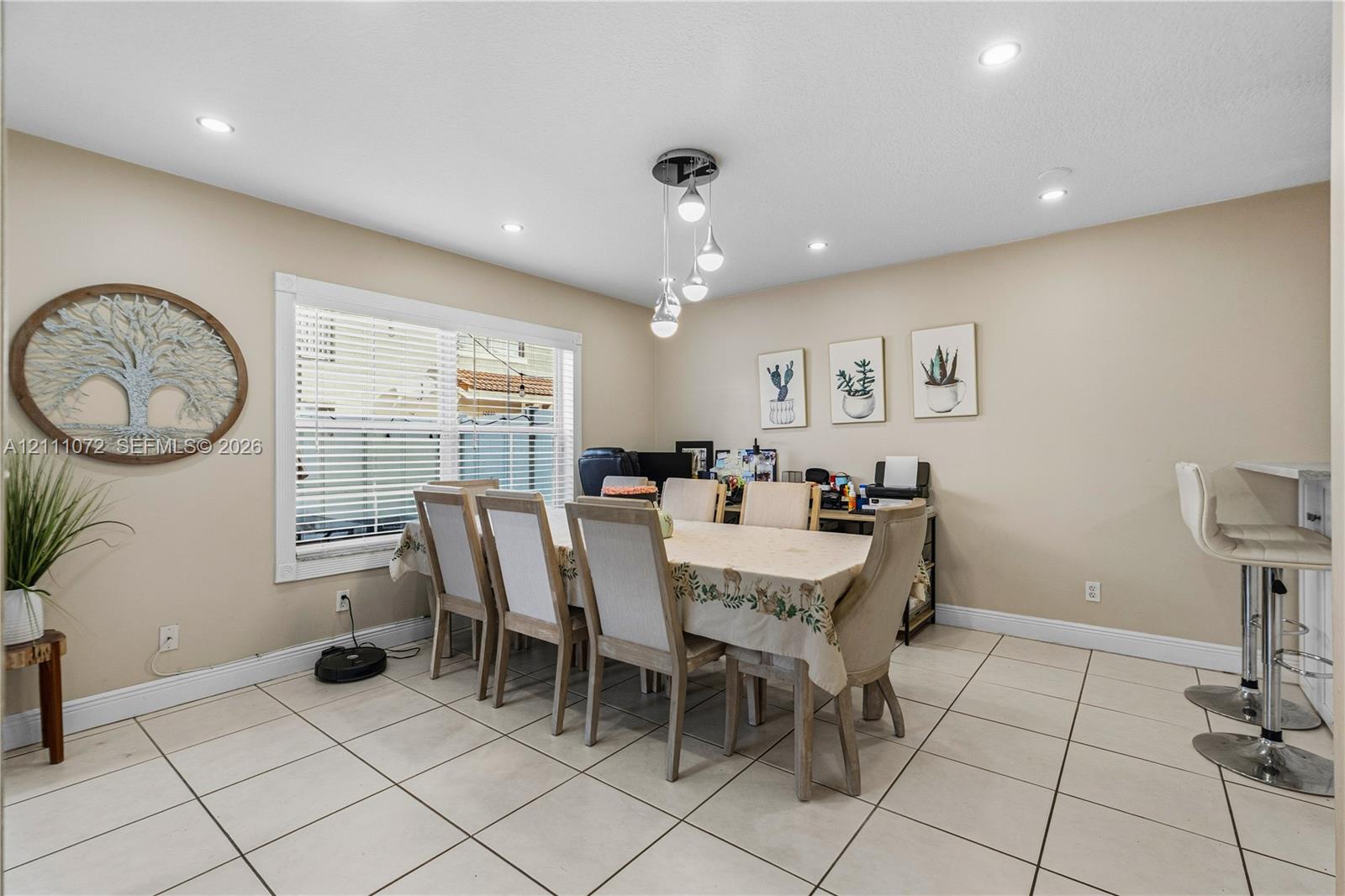 Open-concept room featuring light-toned tile flooring, recessed ceiling lighting, a multi-pendant light fixture, and a large window with horizontal blinds