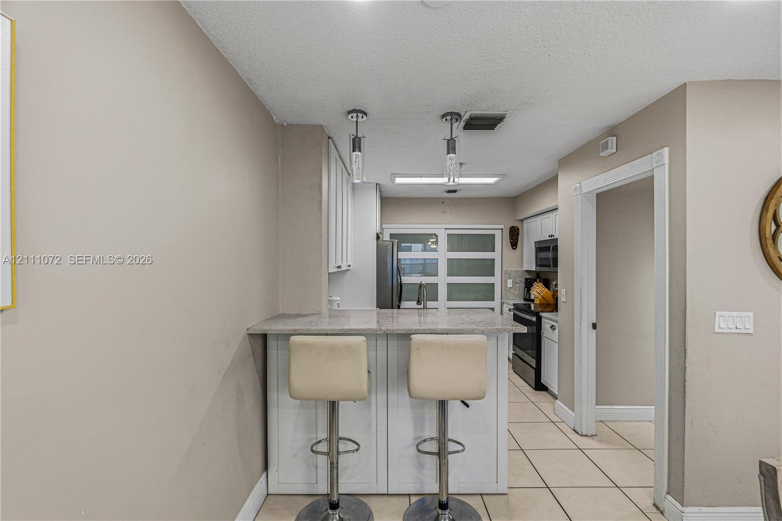 Kitchen featuring a breakfast bar with a stone-surface countertop, white cabinetry, tile flooring, and dual hanging pendant lights