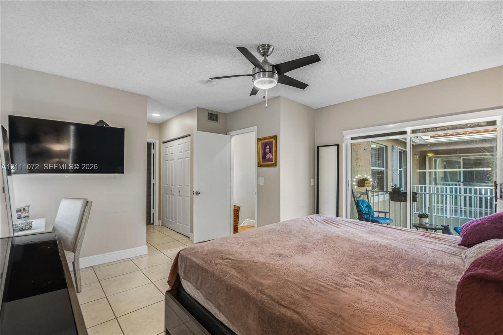 Sliding glass door, neutral tile flooring, built-in ceiling fan with integrated lighting, and multi-panel interior closet doors