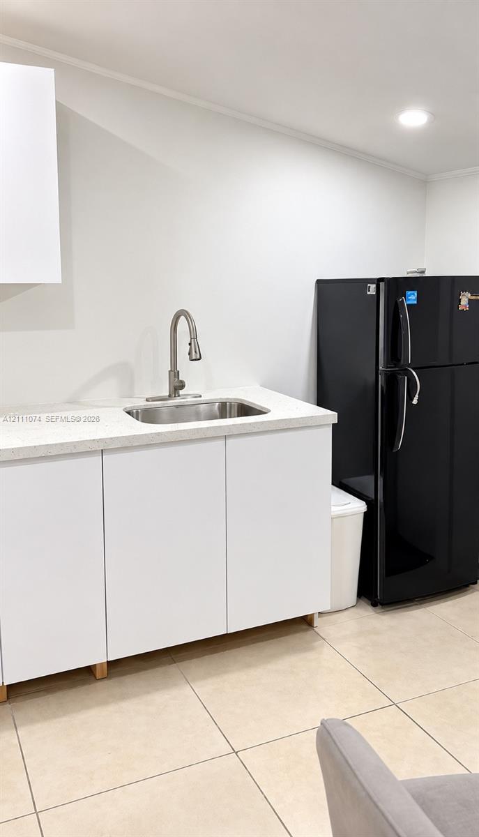 White cabinetry featuring a neutral-toned solid surface countertop, stainless steel undermount sink, brushed nickel high-arc faucet, and large-format tile flooring