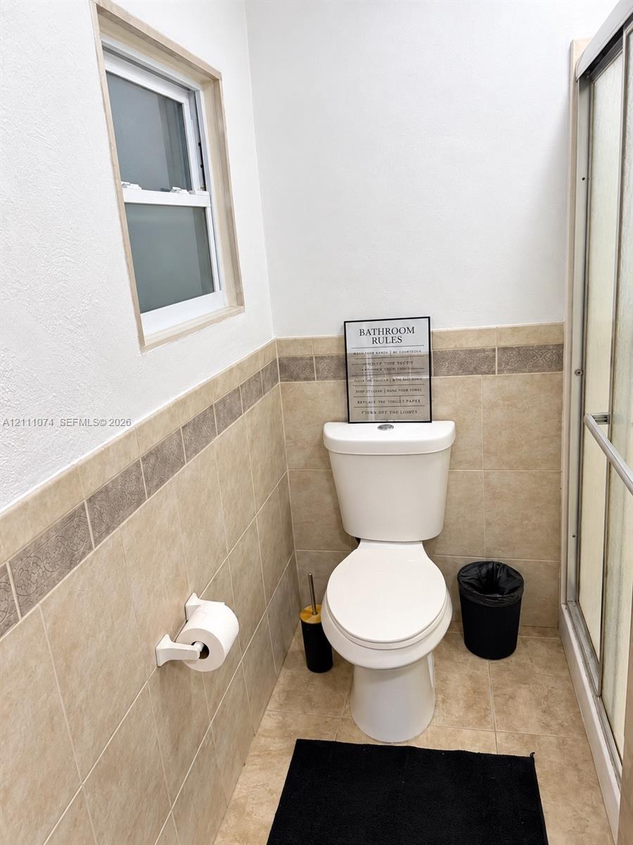 White vanity cabinet with an integrated basin, chrome-finish dual-handle faucet, wall-mounted tilting mirror, and neutral-tone tile wainscoting with decorative accent border