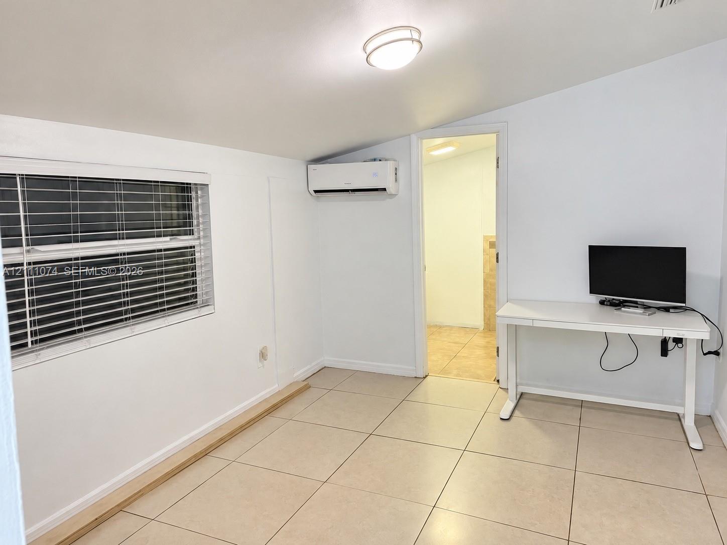 Interior room featuring large-format ceramic tile flooring, a mounted ductless mini-split climate control system, a flush-mount ceiling light fixture, and a window with horizontal blinds