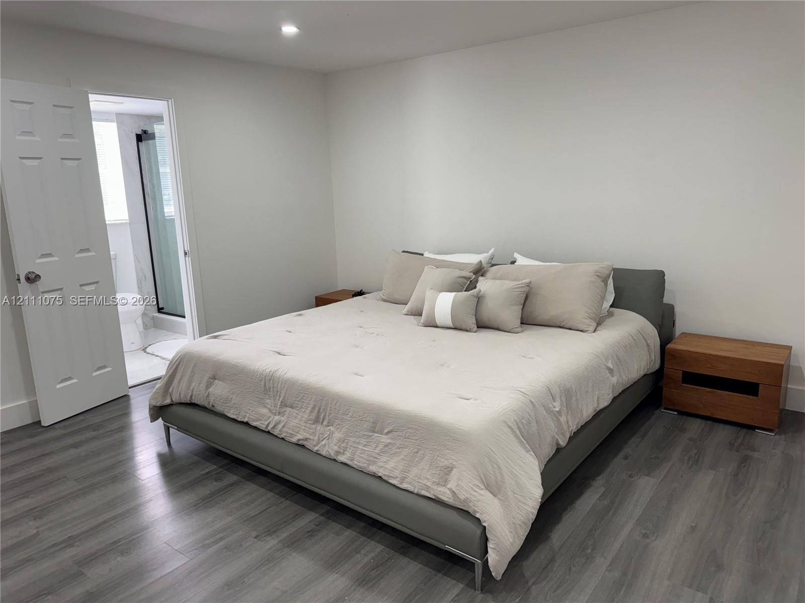 Neutral-toned bedroom featuring wood-finish flooring, recessed lighting, and a six-panel interior door Neutral-toned bedroom featuring wood-finish flooring, recessed lighting, and a six-panel interior door