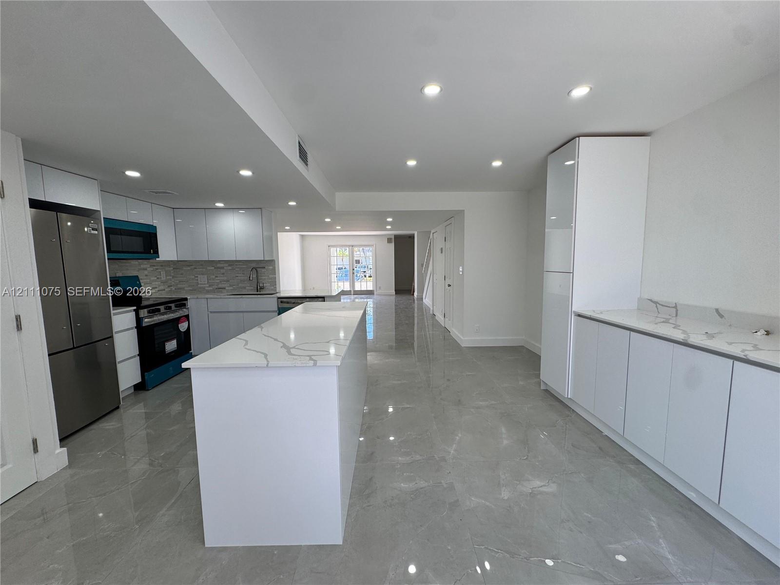 Kitchen featuring white slab-front cabinetry, quartz countertops with gray veining, large-format tile flooring, recessed lighting, and stainless steel appliances Kitchen featuring white slab-front cabinetry, quartz countertops with gray veining, large-format tile flooring, recessed lighting, and stainless steel appliances