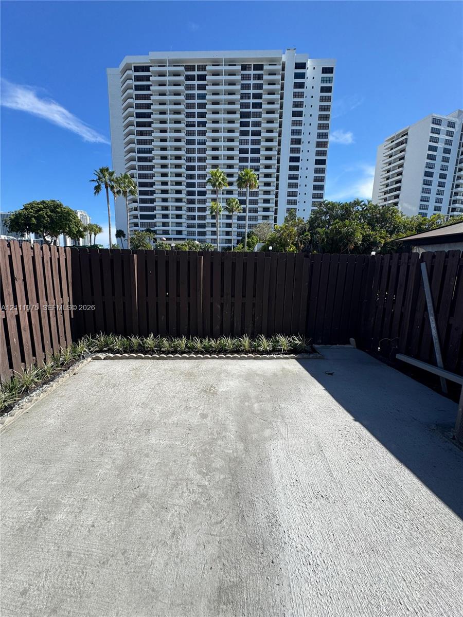 Private concrete patio enclosed by vertical wood fencing, featuring stone-bordered landscape beds