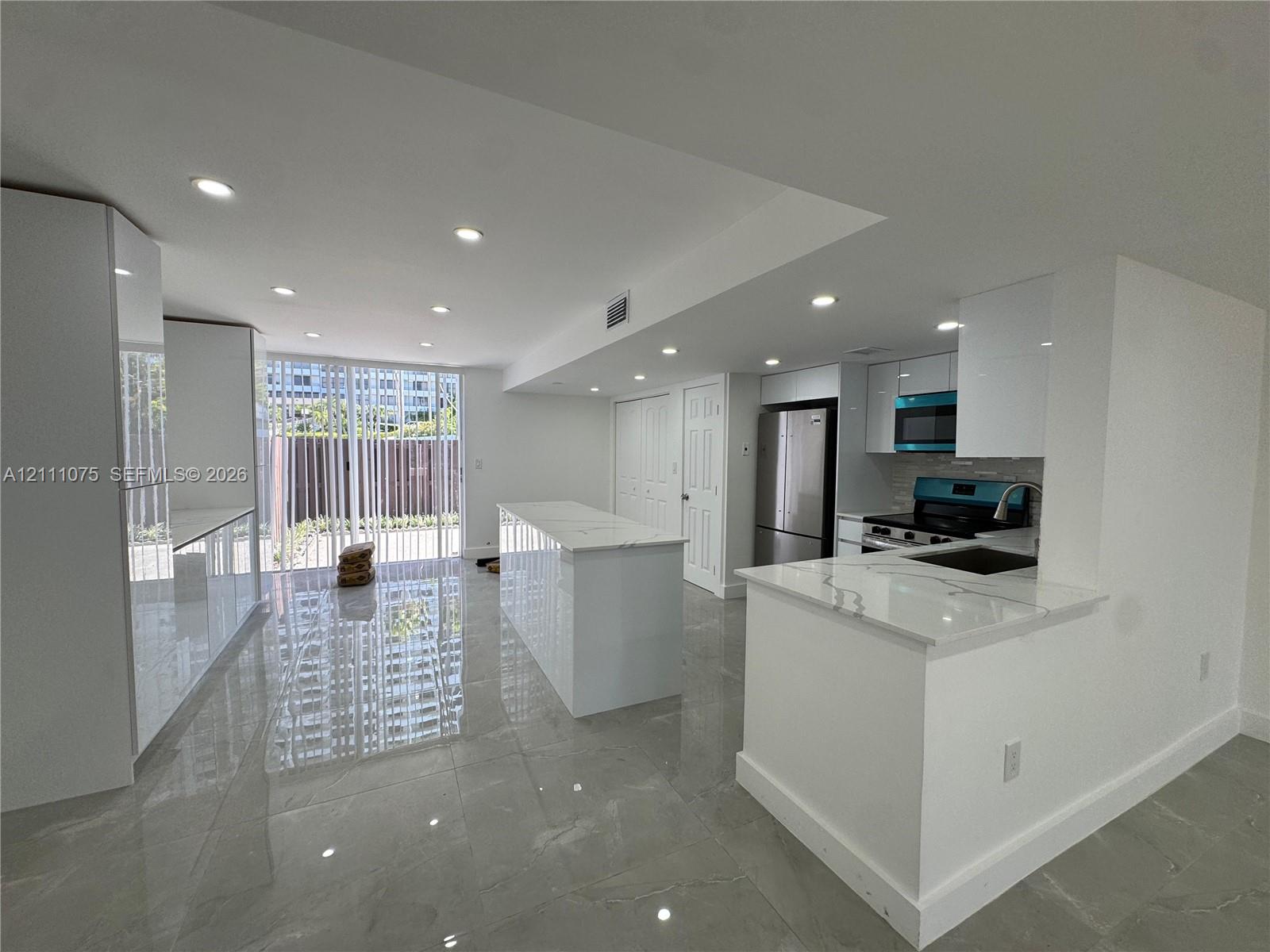 Kitchen featuring white gloss cabinetry, stone-finish countertops, central island, stainless steel appliances, and large-format floor tile Kitchen featuring white gloss cabinetry, stone-finish countertops, central island, stainless steel appliances, and large-format floor tile