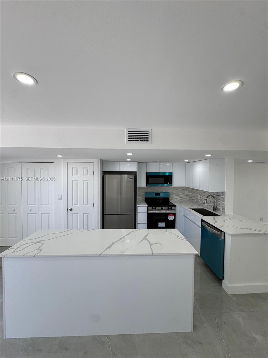 Kitchen featuring white cabinetry, stone-finish countertops with veining, a central island, recessed lighting, and stainless steel appliances Kitchen featuring white cabinetry, stone-finish countertops with veining, a central island, recessed lighting, and stainless steel appliances