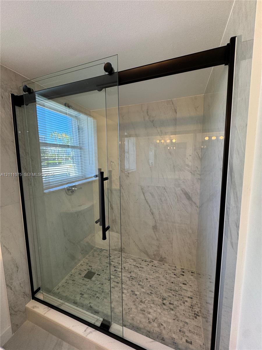 Walk-in shower featuring a sliding glass door with matte black hardware, stone-finish wall tile, and mosaic tile flooring