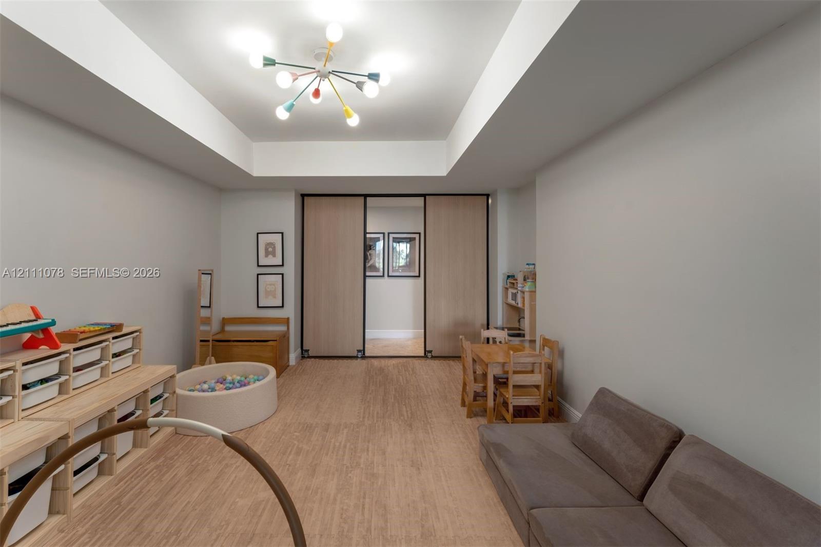 Interior space featuring a recessed tray ceiling, wood-finish flooring, and large sliding doors with dark frames