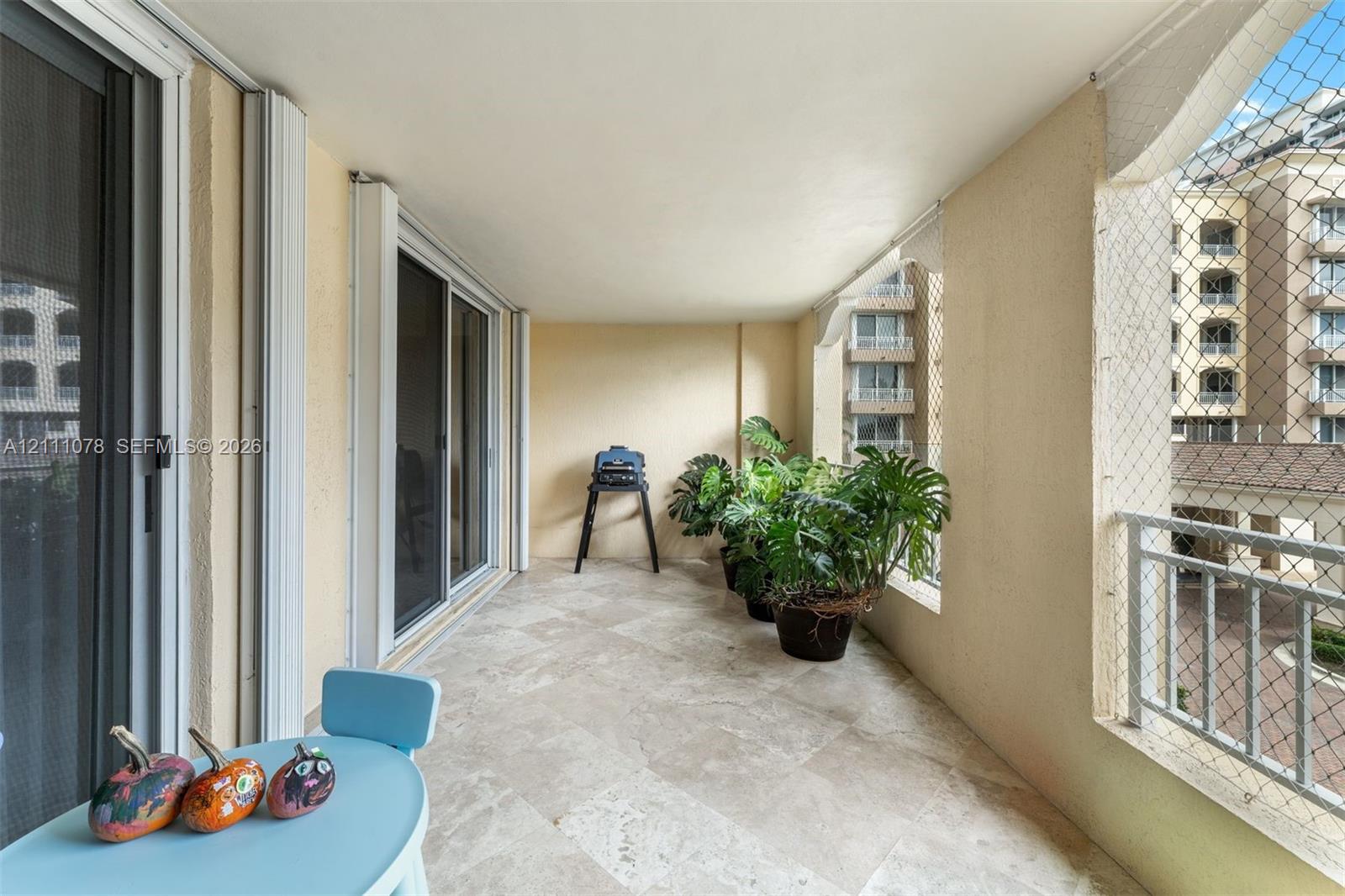 Covered balcony featuring stone flooring, sliding glass door access, and protective mesh screening