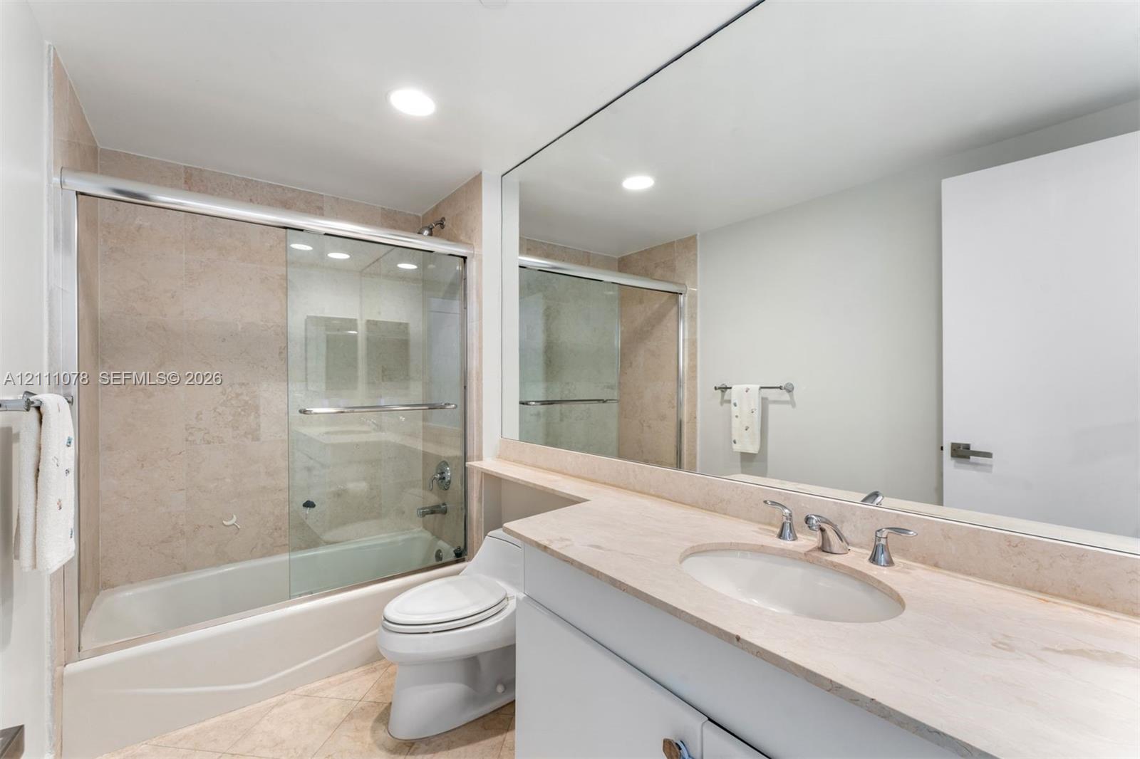 Bathroom featuring a vanity with a stone countertop, an integrated sink, a full-width mirror, and a combination tub and shower enclosure with a sliding glass door