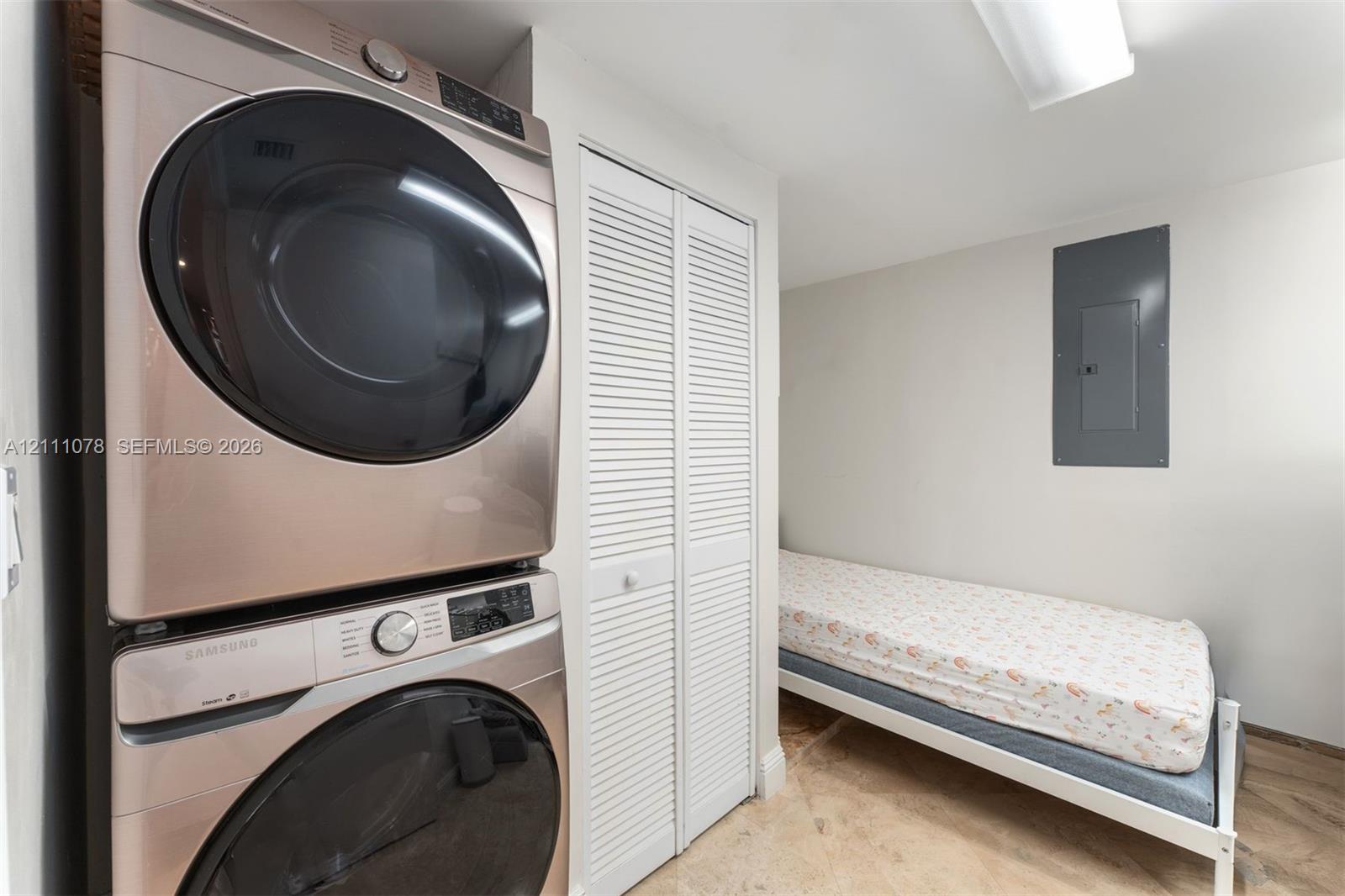 Laundry area featuring a stacked stainless steel front-load washer and dryer set, bifold louvered doors, and stone-finish flooring