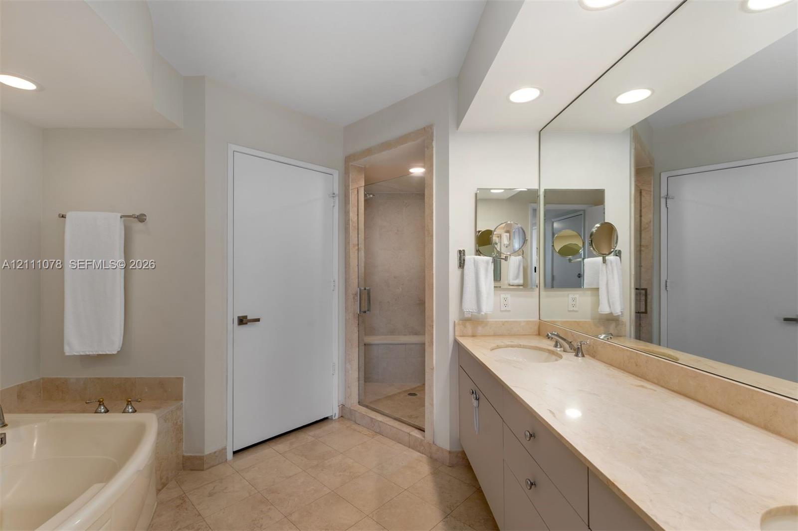 Bathroom featuring a double vanity with a stone countertop, a glass-enclosed shower, a built-in soaking tub with stone surround, and recessed lighting