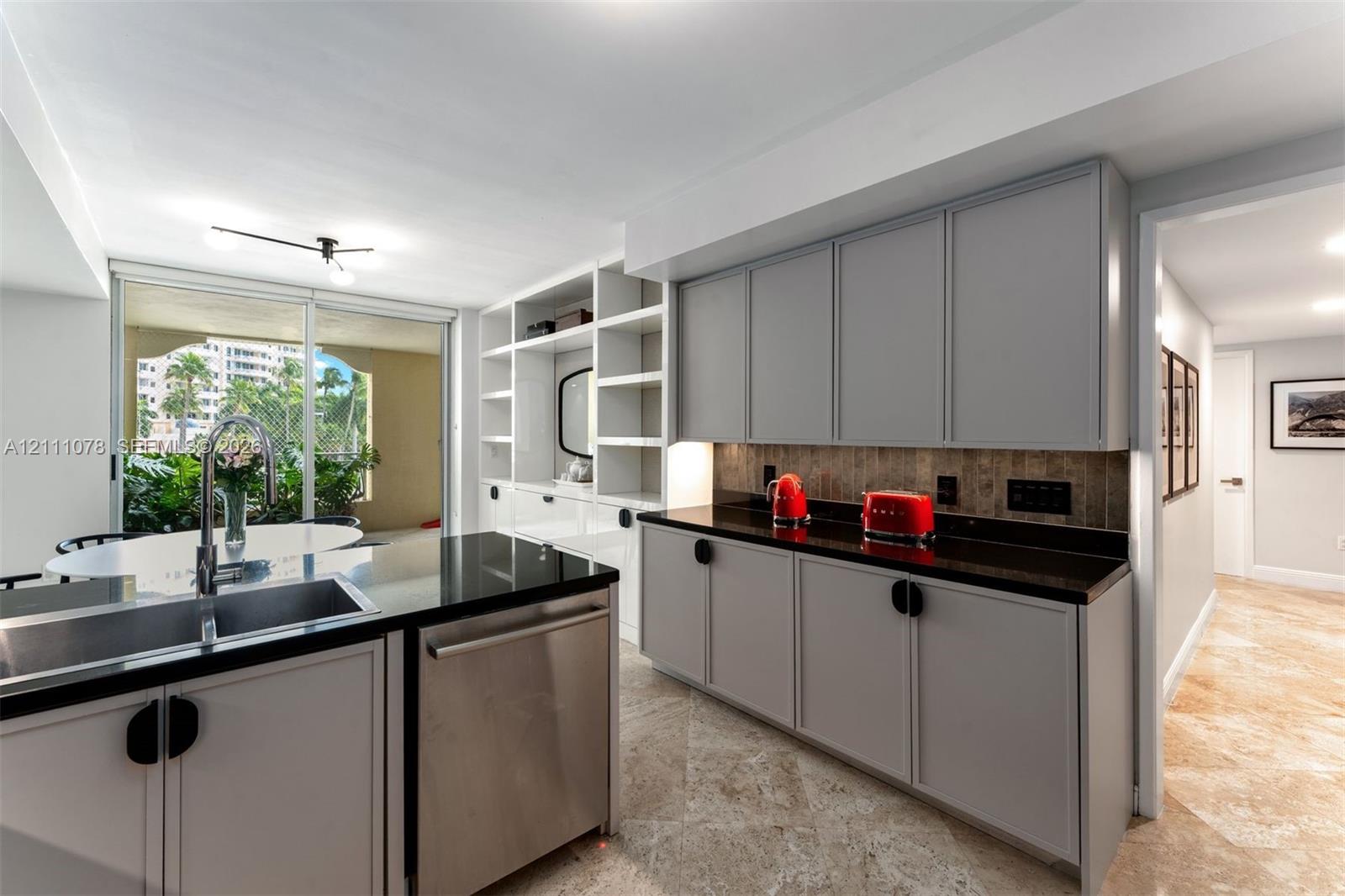 Kitchen featuring grey cabinetry, stone-finish countertops, stainless steel undermount sink, built-in shelving unit, and stone flooring